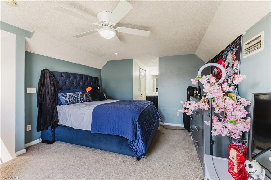 Bedroom featuring carpet flooring, a textured ceiling, ceiling fan, vaulted ceiling, and connected bathroom