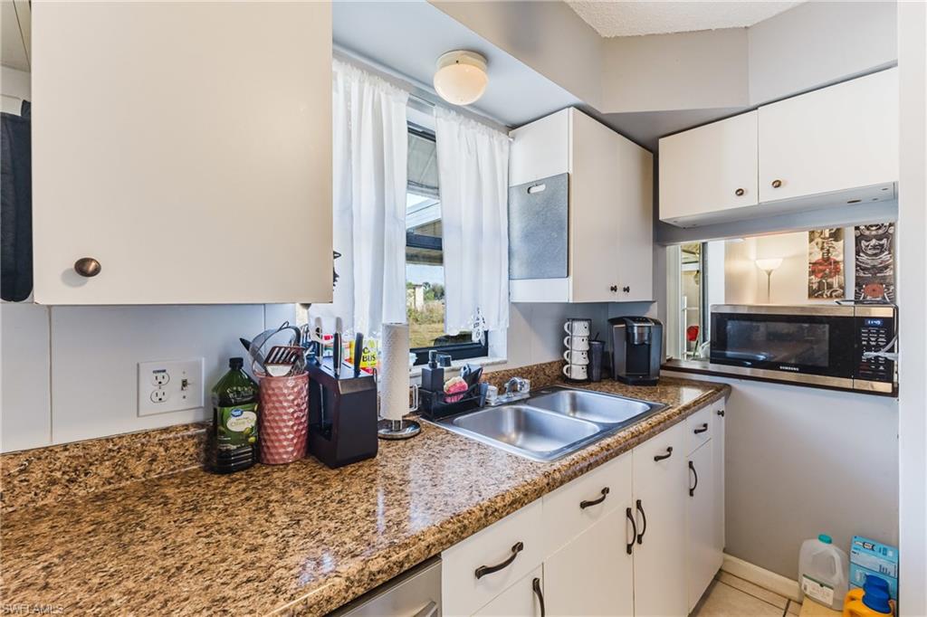 Kitchen featuring white cabinetry, stainless steel microwave, and dark stone countertops