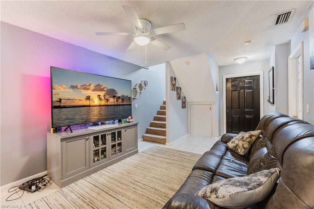 Living area with a textured ceiling, stairway, light tile patterned floors, and a ceiling fan