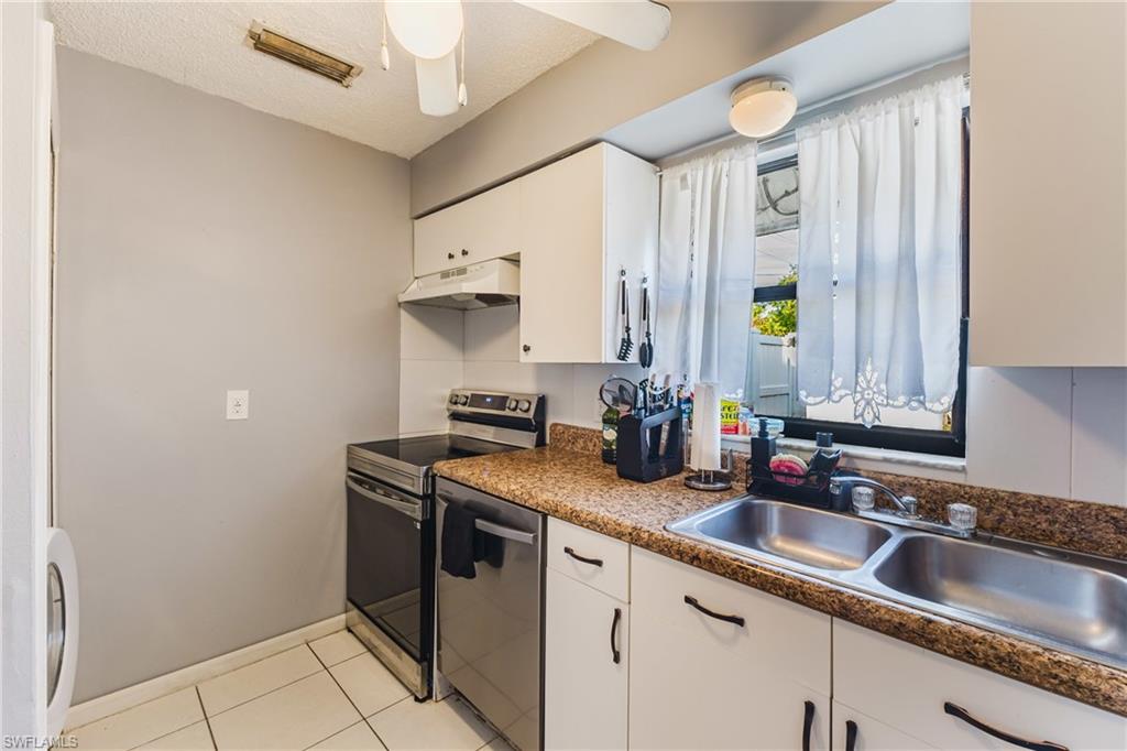 Kitchen with stainless steel appliances, white cabinetry, dark countertops, a textured ceiling, and under cabinet range hood