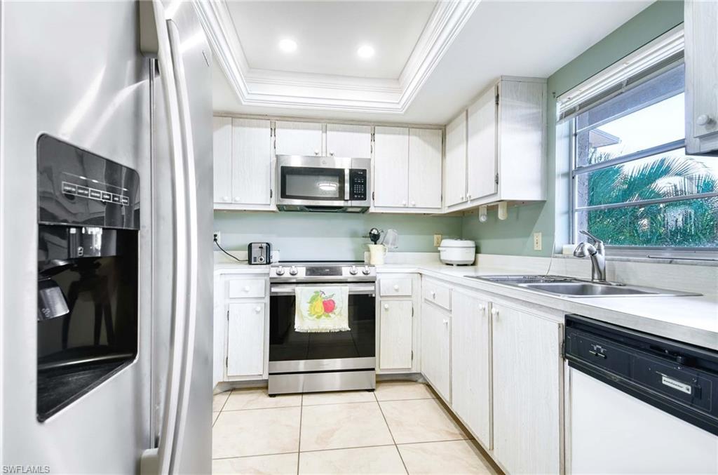 Kitchen with stainless steel appliances, a tray ceiling, light countertops, white cabinetry, and crown molding
