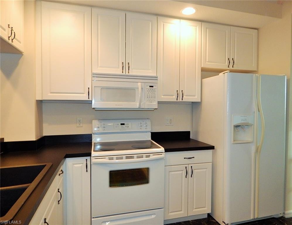 Kitchen with white appliances, white cabinetry, and dark countertops