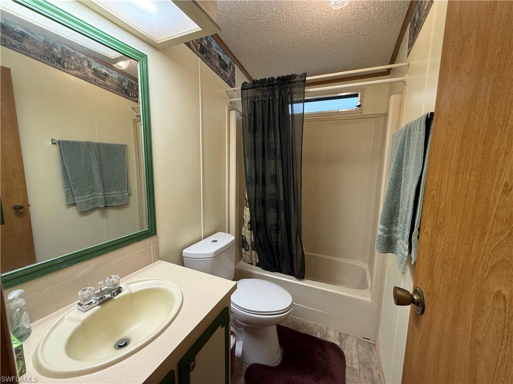 Bathroom with a textured ceiling, shower / tub combo with curtain, vanity, and decorative backsplash