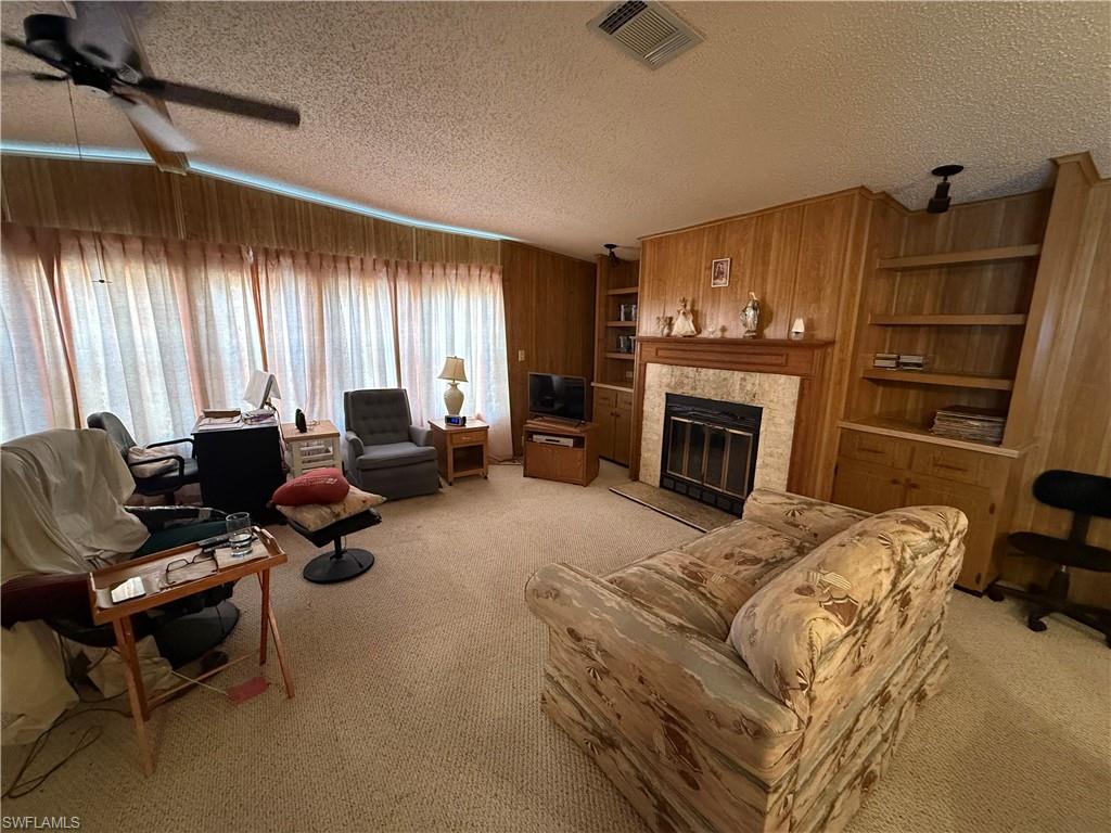 Living room with built in features, a tiled fireplace, light carpet, a textured ceiling, and ceiling fan