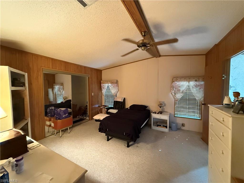 Bedroom with vaulted ceiling, wooden walls, a textured ceiling, light carpet, and ceiling fan