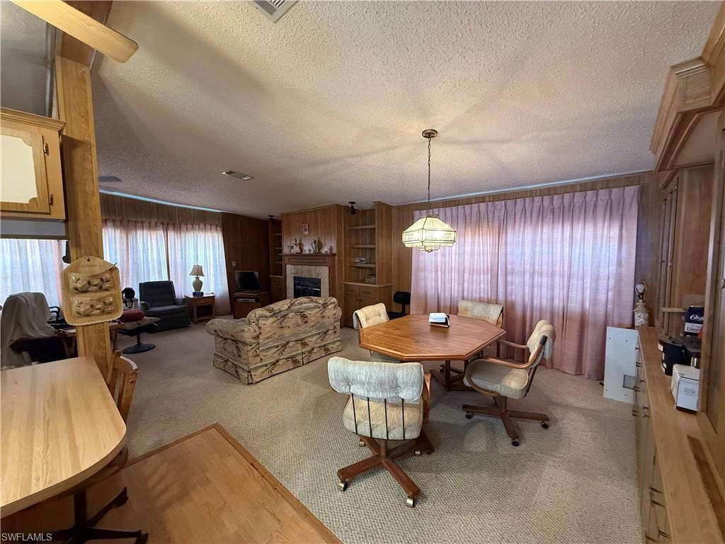 Dining space with a textured ceiling, light colored carpet, a tiled fireplace, and wood walls