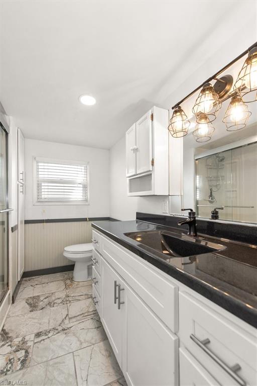 Bathroom with a stall shower, wainscoting, vanity, and light marble finish floors