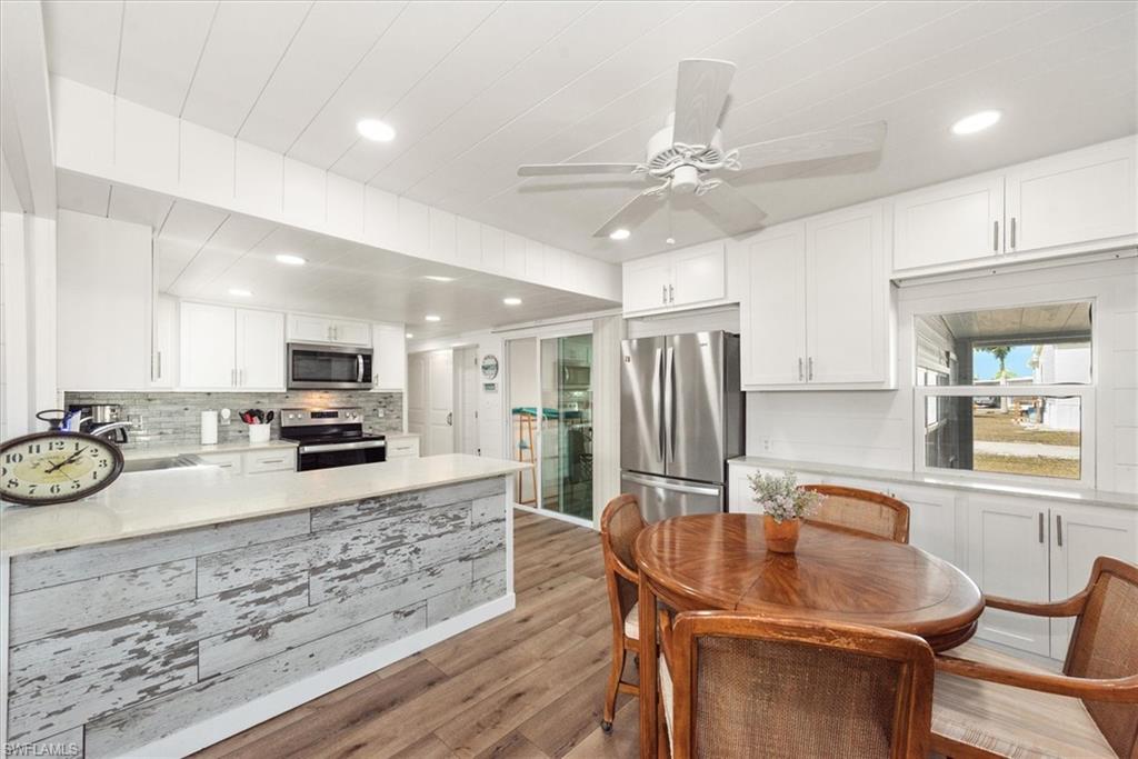 Kitchen with white cabinets, appliances with stainless steel finishes, a peninsula, dark wood-style flooring, and recessed lighting
