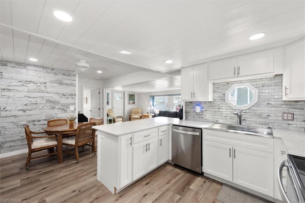 Kitchen featuring white cabinets, a peninsula, stainless steel appliances, wooden walls, and open floor plan