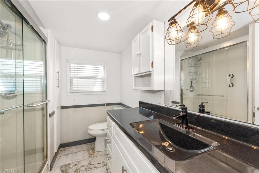 Bathroom with vanity, a stall shower, light marble finish floors, a wainscoted wall, and a chandelier