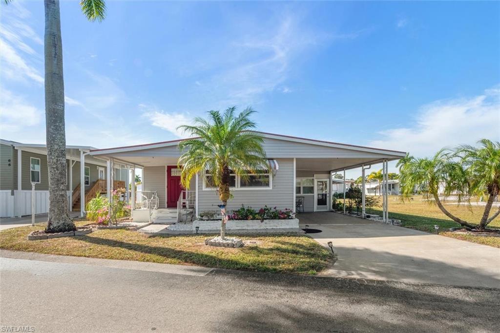 Manufactured / mobile home with concrete driveway, a carport, a front lawn, and covered porch