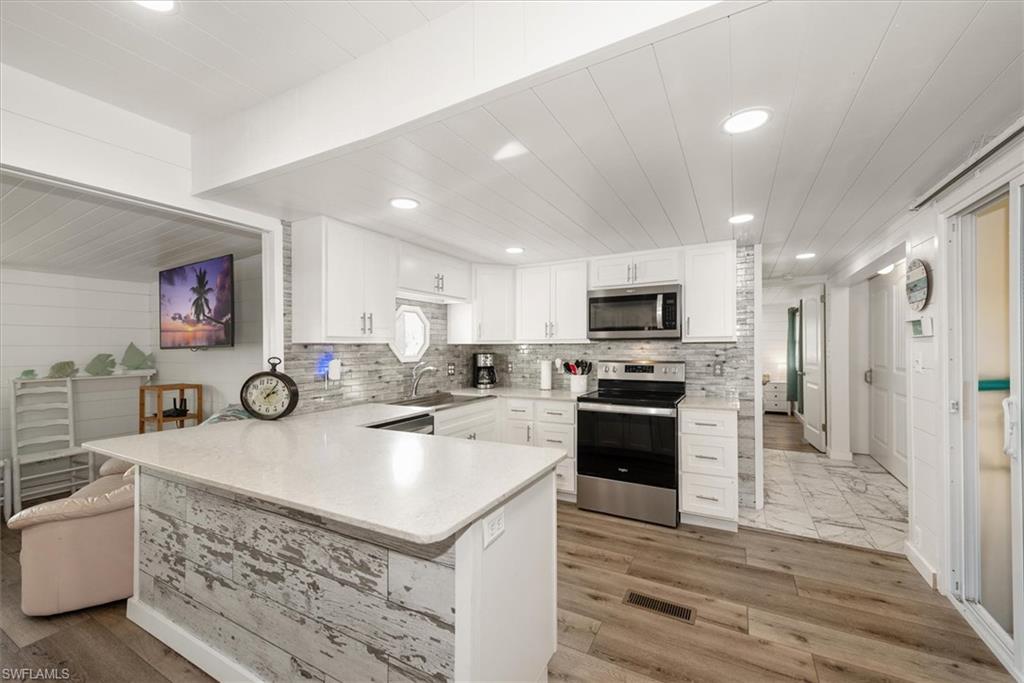 Kitchen with appliances with stainless steel finishes, white cabinets, a peninsula, light stone countertops, and recessed lighting