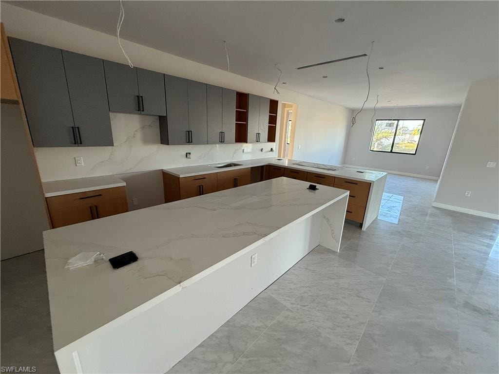 Kitchen featuring a peninsula, light stone countertops, modern cabinets, and light marble finish floors
