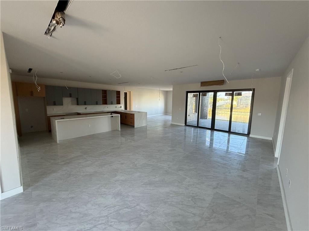 Unfurnished living room featuring baseboards and light marble finish flooring