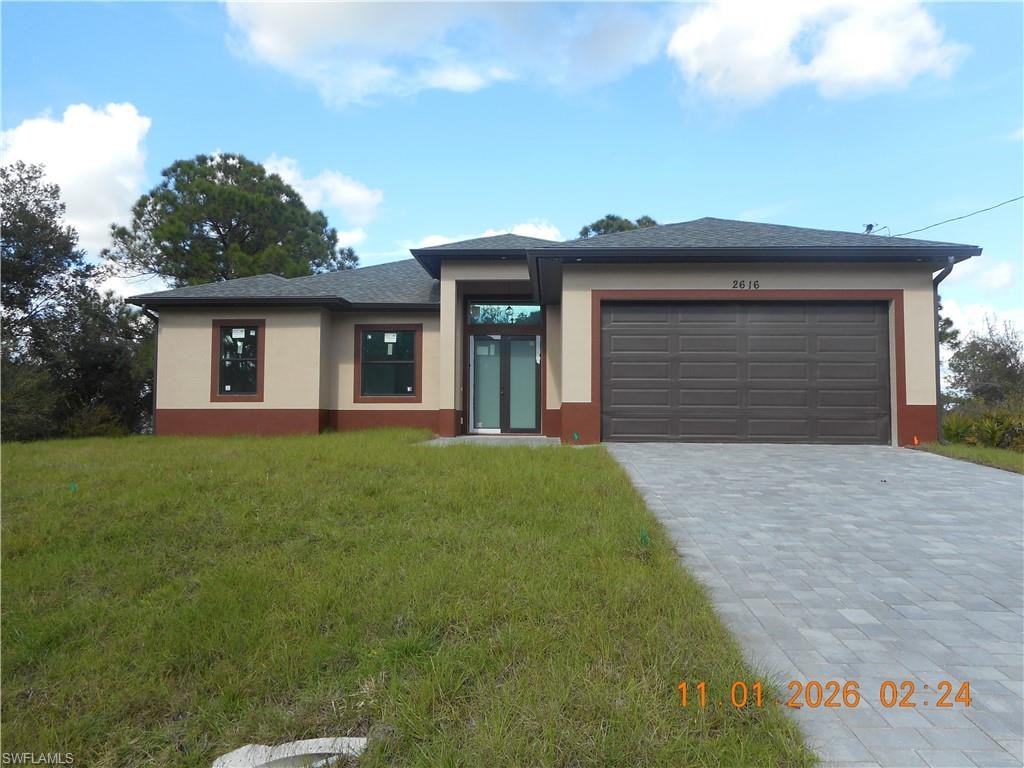 View of front of property featuring stucco siding, a front yard, decorative driveway, a garage, and a shingled roof