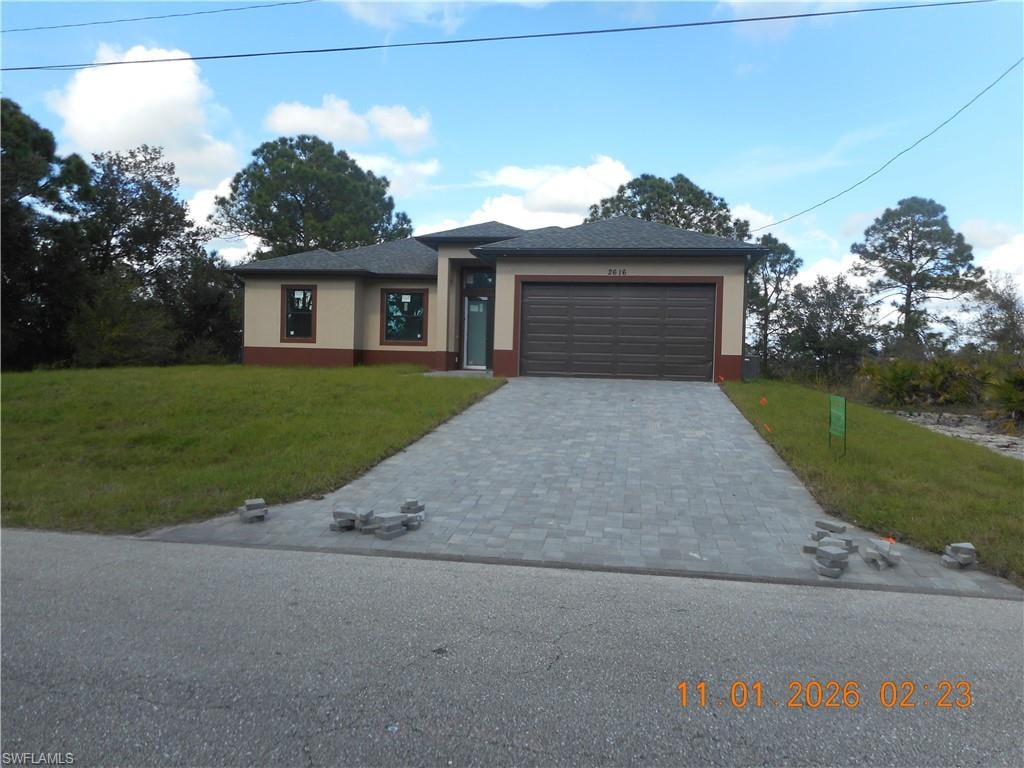 Prairie-style home with a front yard, decorative driveway, stucco siding, and an attached garage