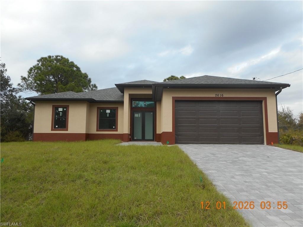 Prairie-style house with decorative driveway, stucco siding, a front yard, and an attached garage