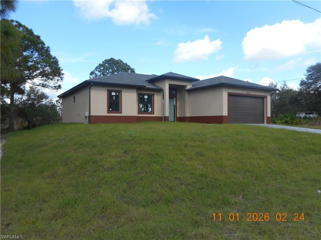 Prairie-style house with an attached garage, a front yard, stucco siding, and driveway