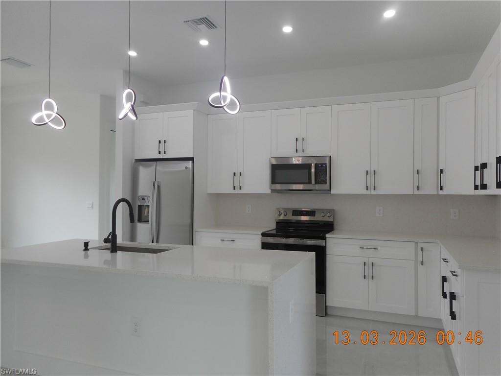 Kitchen featuring stainless steel appliances, light stone countertops, white cabinets, and a kitchen island with sink