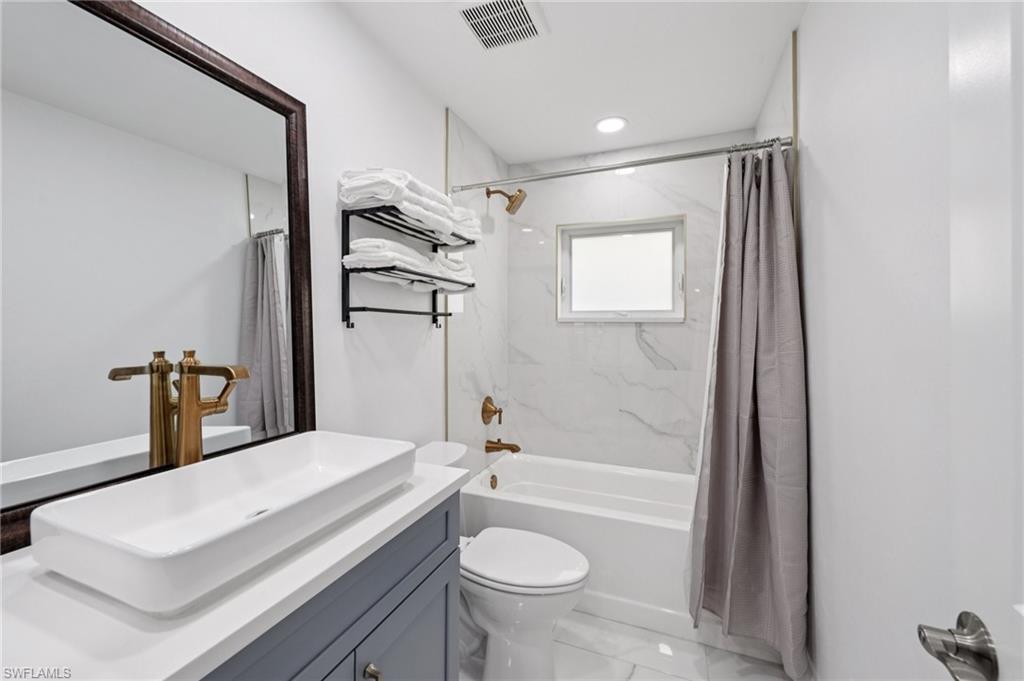 Bathroom with vanity, shower / bath combination with curtain, light marble finish floors, and recessed lighting
