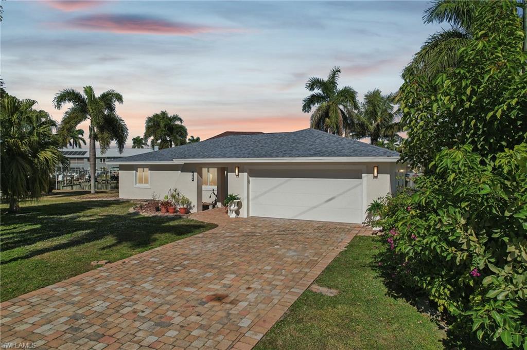 Ranch-style home featuring stucco siding, a front lawn, decorative driveway, a garage, and roof with shingles