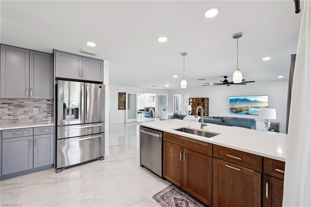 Kitchen with appliances with stainless steel finishes, open floor plan, decorative light fixtures, light marble finish floors, and decorative backsplash