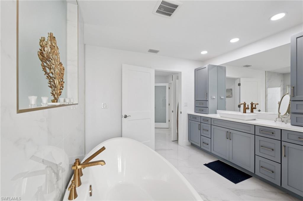 Bathroom featuring a freestanding tub, light marble finish floors, vanity, and recessed lighting