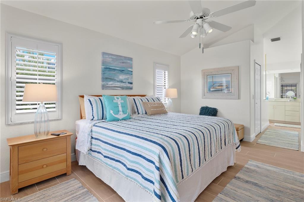 Bedroom featuring lofted ceiling, light hardwood / wood-style floors, ensuite bath, and ceiling fan