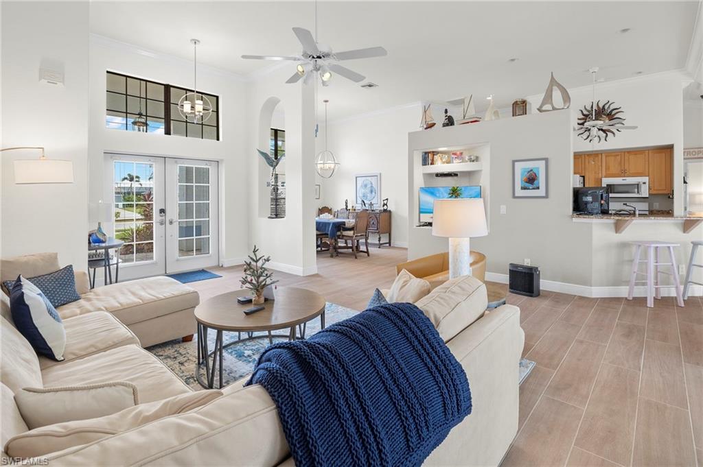 Living room with light hardwood / wood-style floors, ornamental molding, french doors, and ceiling fan with notable chandelier