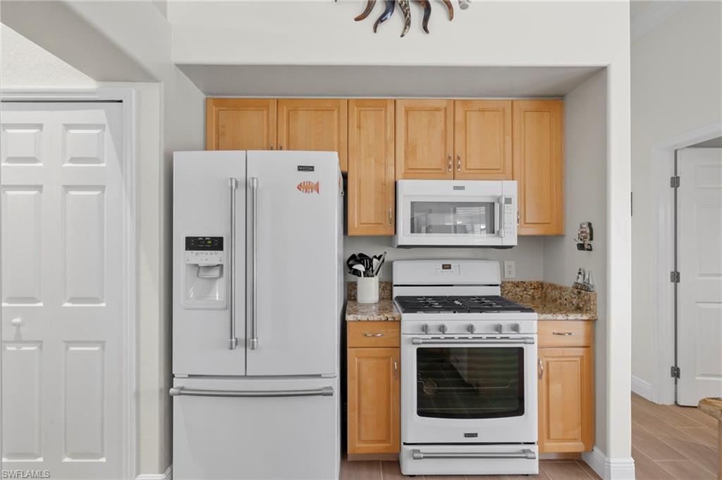 Kitchen with light brown cabinets, white appliances, light wood-type flooring, and light stone counters