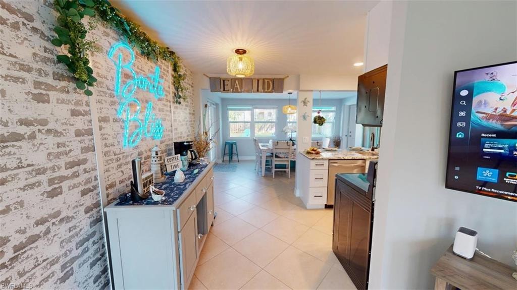Kitchen featuring brick wall, pendant lighting, stainless steel dishwasher, dark stone countertops, and light tile patterned floors