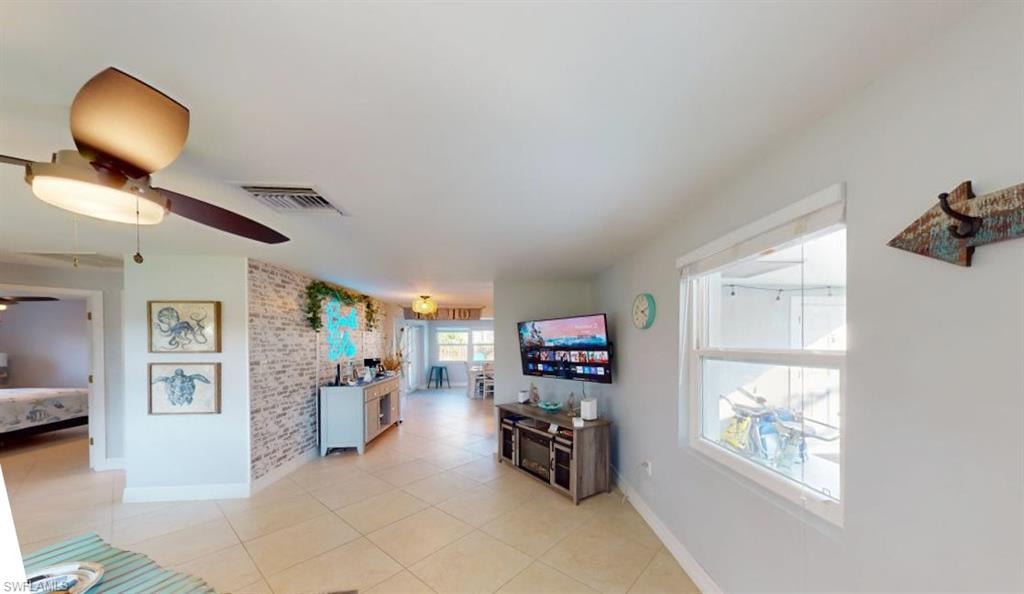 Living area with light tile patterned flooring, brick wall, and ceiling fan