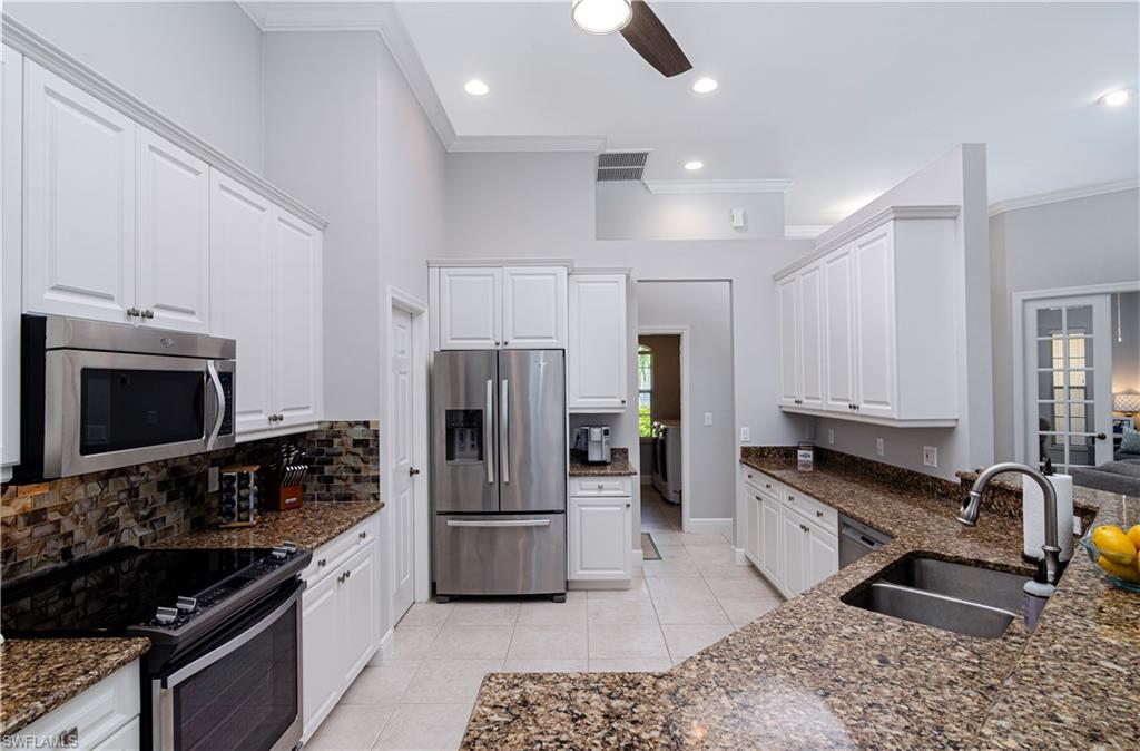 Kitchen with sink, light tile patterned floors, appliances with stainless steel finishes, white cabinetry, and dark stone countertops