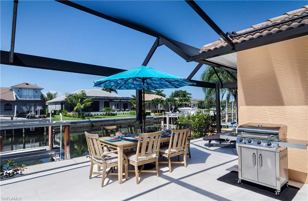 View of patio with area for grilling, a water view, and glass enclosure
