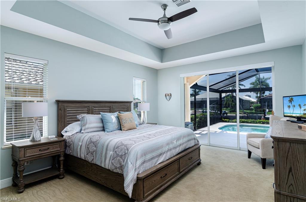 Carpeted bedroom with ceiling fan, a raised ceiling, and access to outside