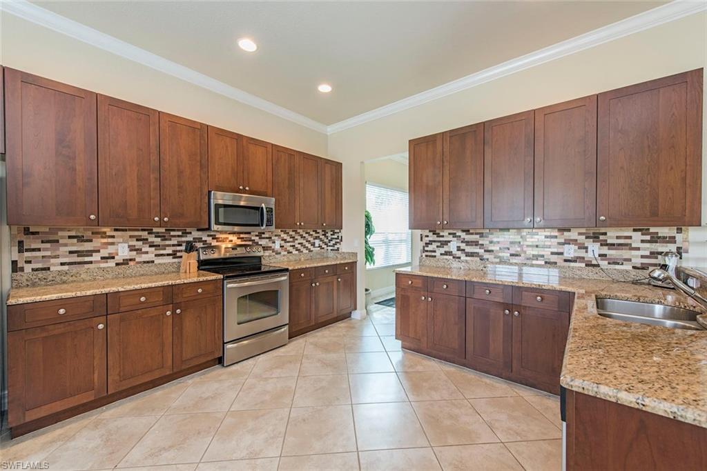 Kitchen with appliances with stainless steel finishes, light stone counters, ornamental molding, light tile patterned floors, and tasteful backsplash