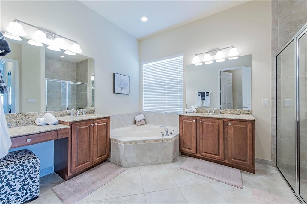 Bathroom with a bath, a shower stall, two vanities, and light tile patterned floors