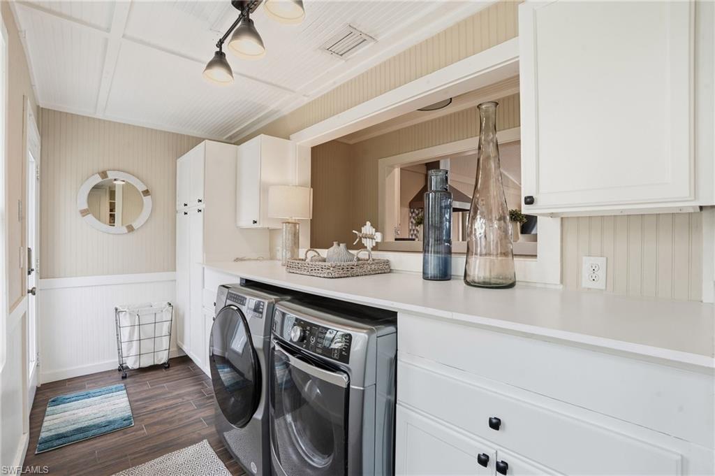Laundry area with wood finish floors, washing machine and clothes dryer, cabinet space, wainscoting, and wooden walls - Virtually Edited Image