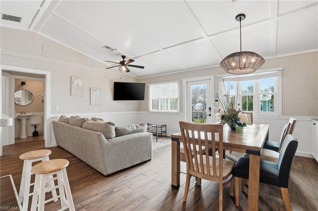 Dining area featuring wood finished floors, lofted ceiling, a ceiling fan, a wainscoted wall, and a chandelier - Virtually Edited Image