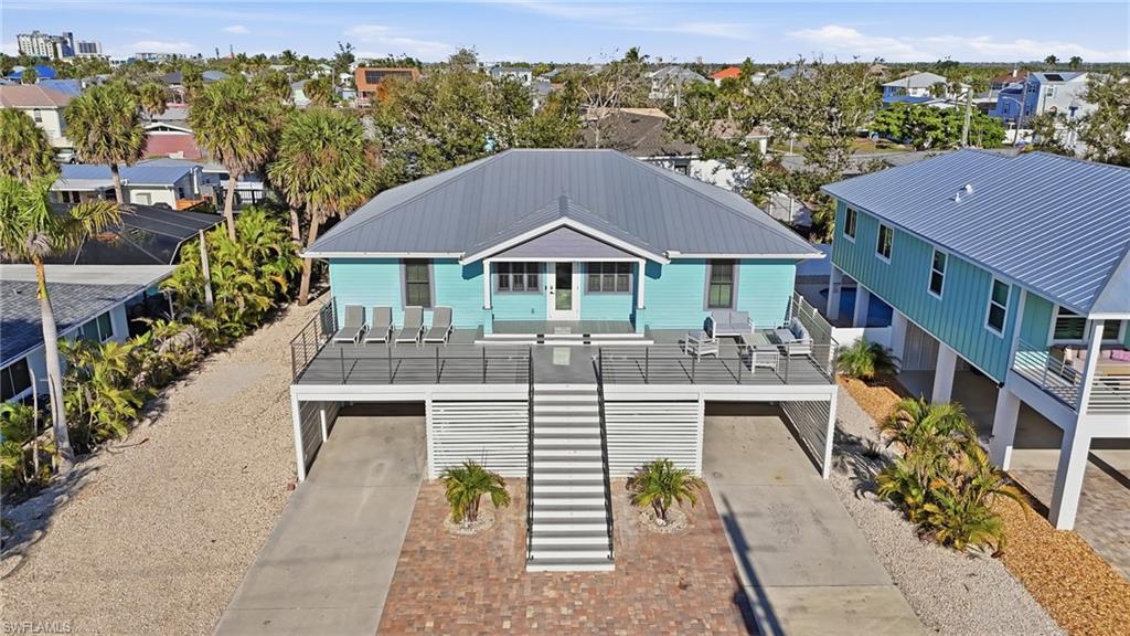 Coastal inspired home featuring stairway, a garage, a balcony, driveway, and a metal roof - Virtually Edited Image