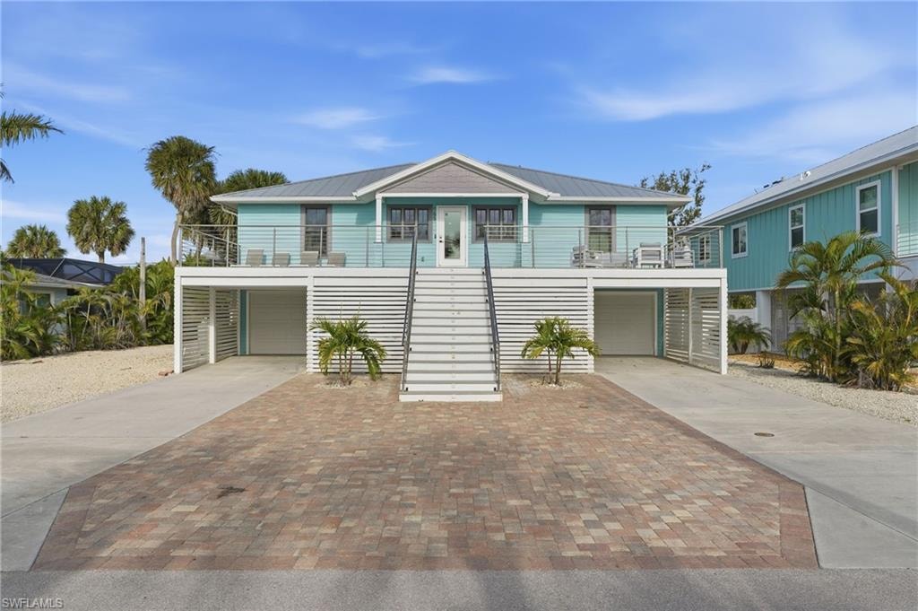 Coastal inspired home featuring stairway, a garage, a balcony, driveway, and a metal roof - Virtually Edited Image