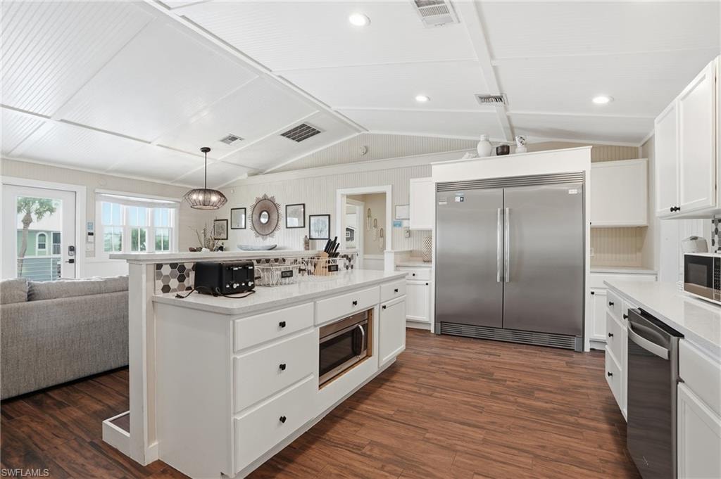 Kitchen featuring stainless steel appliances, white cabinets, open floor plan, lofted ceiling, and pendant lighting - Virtually Edited Image