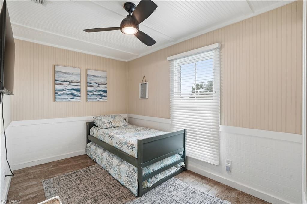 Bedroom featuring wainscoting, wood finished floors, ceiling fan, crown molding, and wallpapered walls - Virtually Edited Image