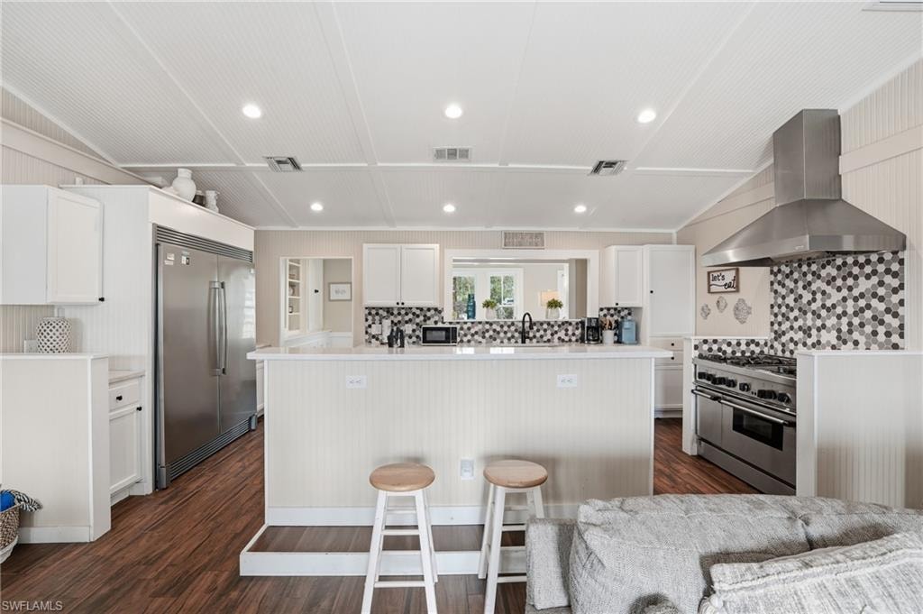 Kitchen with wall chimney exhaust hood, white cabinets, high quality appliances, recessed lighting, and decorative backsplash - Virtually Edited Image