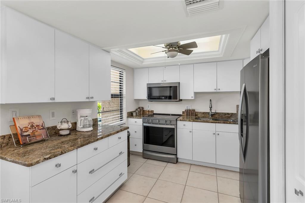 Kitchen with appliances with stainless steel finishes, dark stone countertops, white cabinets, and a tray ceiling