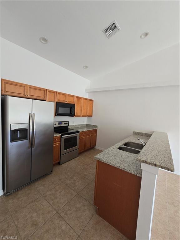 Kitchen featuring black range oven, fridge, light stone counters, brown cabinets, and a peninsula