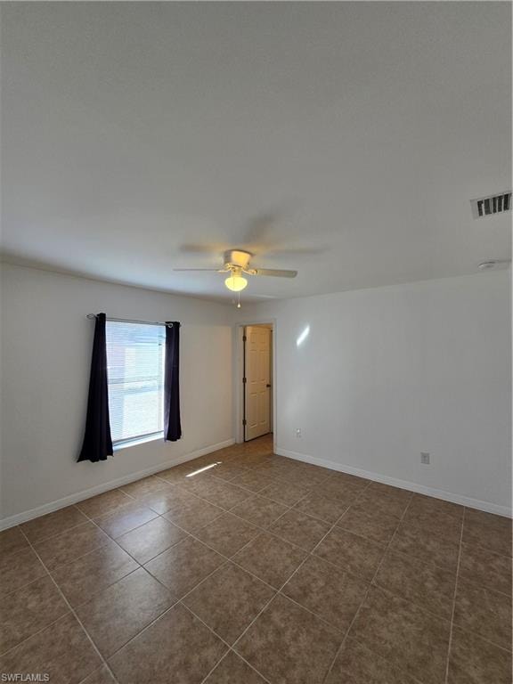 Tiled spare room featuring a ceiling fan and baseboards