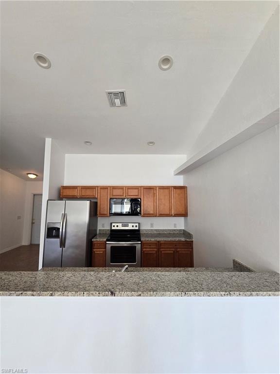 Kitchen with stove, brown cabinetry, refrigerator, recessed lighting, and dark stone countertops