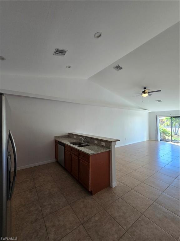 Kitchen featuring a peninsula, refrigerator, vaulted ceiling, dark tile patterned flooring, and brown cabinets