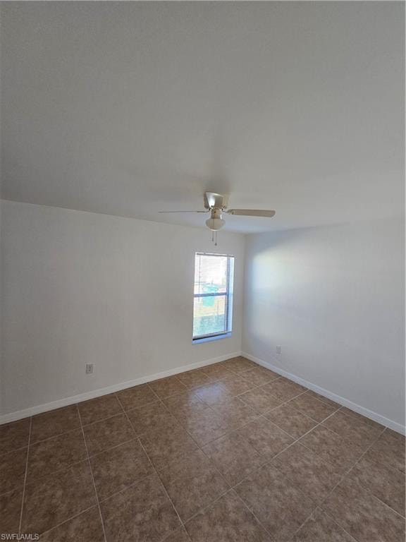 Tiled empty room with a ceiling fan and baseboards